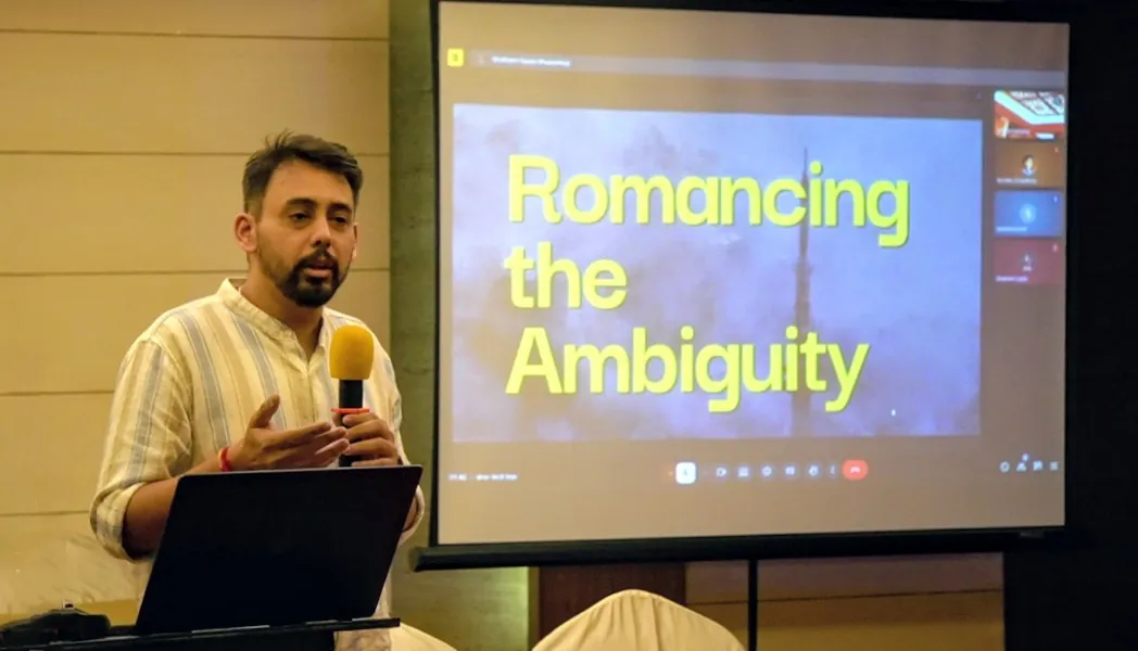 Shubham Gupta speaking beside a screen displaying Romancing the Ambiguity.